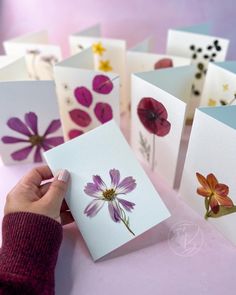 a person is holding some cards with flowers on them in front of a pink background