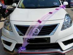 a white car with a purple ribbon tied to it's front bumper and hood