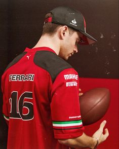 a man holding a football in his right hand and wearing a red jersey with the number 16 on it