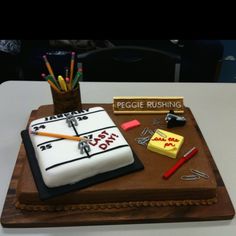 a cake with writing on it sitting on top of a white table next to some pens and pencils