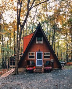 a - frame cabin nestled in the woods surrounded by trees and flowers with fall foliage