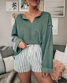 a woman standing in front of a couch wearing green sweater and striped shorts with her hands on her hips