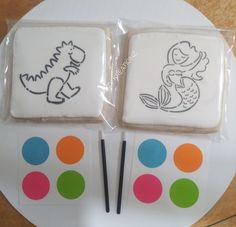 two decorated cookies sitting on top of a white plate next to markers and stickers