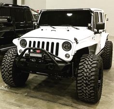 a white jeep parked in a garage next to another black truck with its lights on