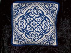 a blue and white knitted pillow sitting on top of a black velvet couch cushion