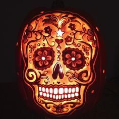 a lit up pumpkin with a skull on it's face and flowers in the center