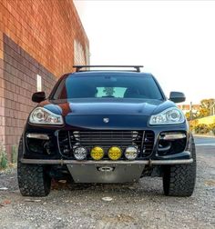 the front end of a black car parked in front of a brick building with its lights on