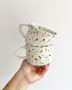 two hand holding up three cups with stars on them, one is white and the other is multicolored