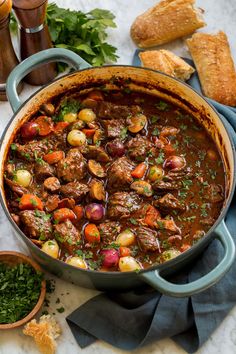 a large pot filled with stew next to bread and other food on a table top