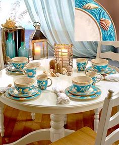 a white table topped with lots of blue cups and saucers next to a window