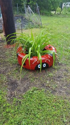 a red planter with eyes painted on it in the grass next to a tree