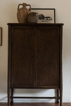 a wooden cabinet sitting on top of a hard wood floor next to a white wall