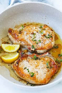 two pieces of chicken in a white bowl with lemon wedges and parsley on the side