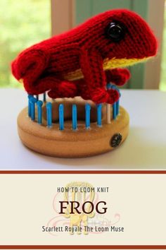 a red knitted frog sitting on top of a wooden stand with pins in it