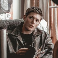 a man sitting in a chair holding a book and looking at the camera with an intense look on his face