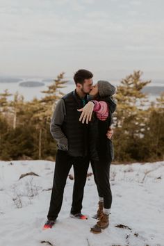 a man and woman standing in the snow with their arms around each other as they kiss