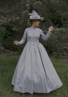 This Halloween, experience the allure of wearing this grey cotton dress - a true Victorian cut. From the tailored fit of the straight cut bodice to the modest high collar neckline and long tapered set sleeves, this dress is perfect! The graceful four-paneled skirt is full enough to accommodate a hoop or petticoat. Front button closure with metal button accents. What a delightful dress! Hand wash or machine wash gently. Tumble dry. 100% cotton. Liesa is wearing an extra full crinoline, grey witch 1880 Dress, Grey Cotton Dress, Victorian Dress Gown, Grey Witch, Hedda Gabler, Fashion Eras, Victorian Era Dresses, 1800's Dress, Making A Wedding Dress