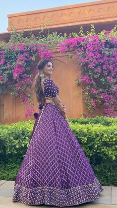 a woman in a purple and black dress is standing near some bushes with pink flowers