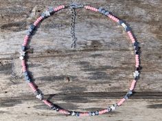 a pink and blue beaded necklace sitting on top of a wooden table next to a piece of wood