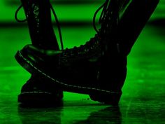 a pair of black combat boots sitting on top of a wooden floor in front of a green wall