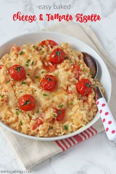 a white bowl filled with rice and tomatoes on top of a table next to a spoon