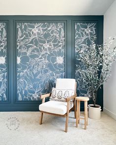 a chair sitting in front of a blue wall with flowers on it and a potted plant