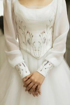 a woman in a white dress with flowers on it's sleeves and arms, wearing a tiara