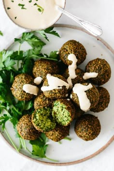 a white plate topped with falafel next to a bowl of ranch dressing