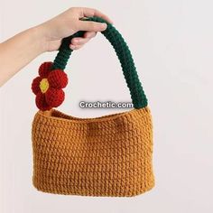 a hand holding a crocheted purse with a flower on the handle and handles