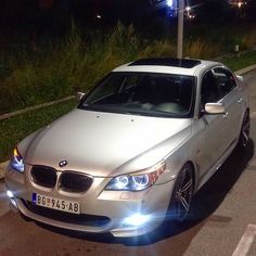 a silver car is parked on the side of the road at night with its lights on