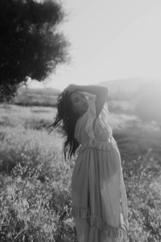 a woman standing in a field with her arms behind her head