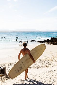 a man holding a surfboard on the beach with people in the water behind him