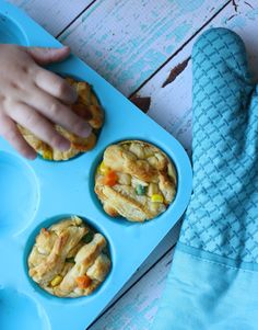 a blue tray filled with muffins next to a child's hand and glove