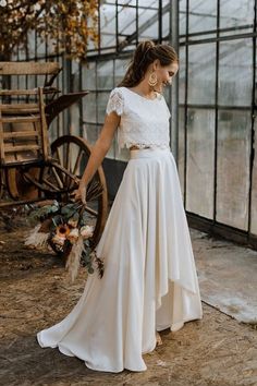 a woman standing in front of a greenhouse wearing a white dress and holding a bouquet