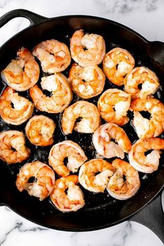 shrimp being cooked in a skillet on top of a marble countertop with utensils