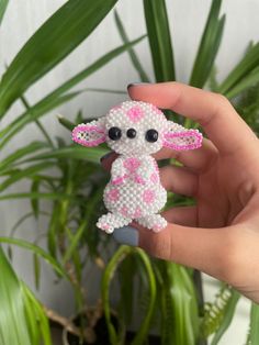 a hand holding a small beaded animal in front of a potted plant