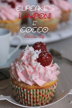 cupcakes with pink frosting and raspberries are on a white plate