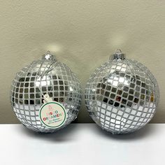 two shiny disco ball ornaments sitting on top of a white table next to each other