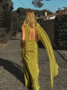 a woman in a yellow dress is walking down the street with her back to the camera