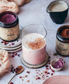 three jars filled with different colored powders on top of a white table next to spoons