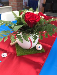 a red rose in a baseball themed vase on a table with green grass and balls