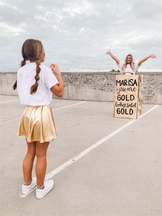 two girls are standing in an empty parking lot and one girl is holding a sign