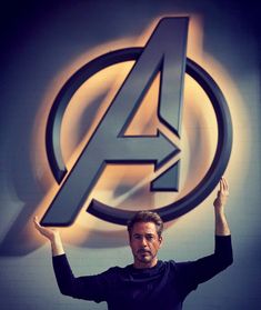 a man holding his hands up in front of the avengers logo with an arrow above it