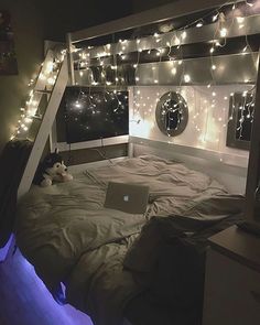 a bed with a laptop on top of it in a room that has lights strung from the ceiling