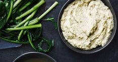 some green vegetables and dip in bowls on a table