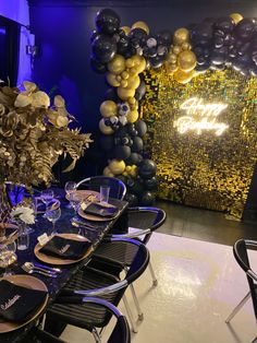 a table set up for a party with black and gold balloons on the wall behind it