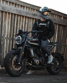 a man sitting on top of a motorcycle next to a wooden fence and wearing a helmet