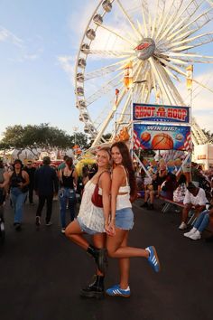 two women standing next to each other in front of a ferris wheel