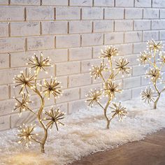 three small plants with lights on them sitting in front of a brick wall and snow