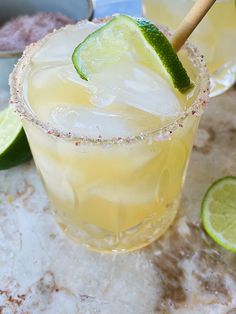 two glasses filled with lemonade and limes on top of a marble countertop